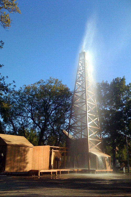 Modern re-enactment of oil gusher using water at wooden derrick.