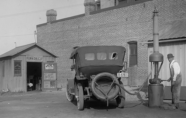 An early gas station attendant fills a n auto gas tank.