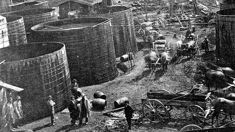 Large wooden oil tanks and 42-gallon barrels with nearby teamsters.
