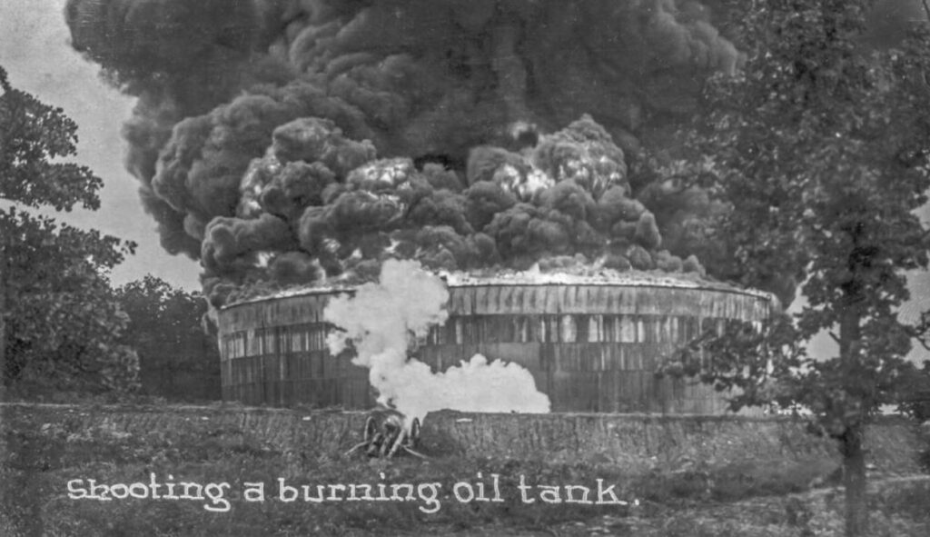 Cannon shoots burning oil tank, circa 1915.