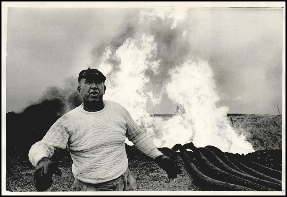 Myron Kinley in fireproof coat and gloves with flaming well dangerously close behind him.
